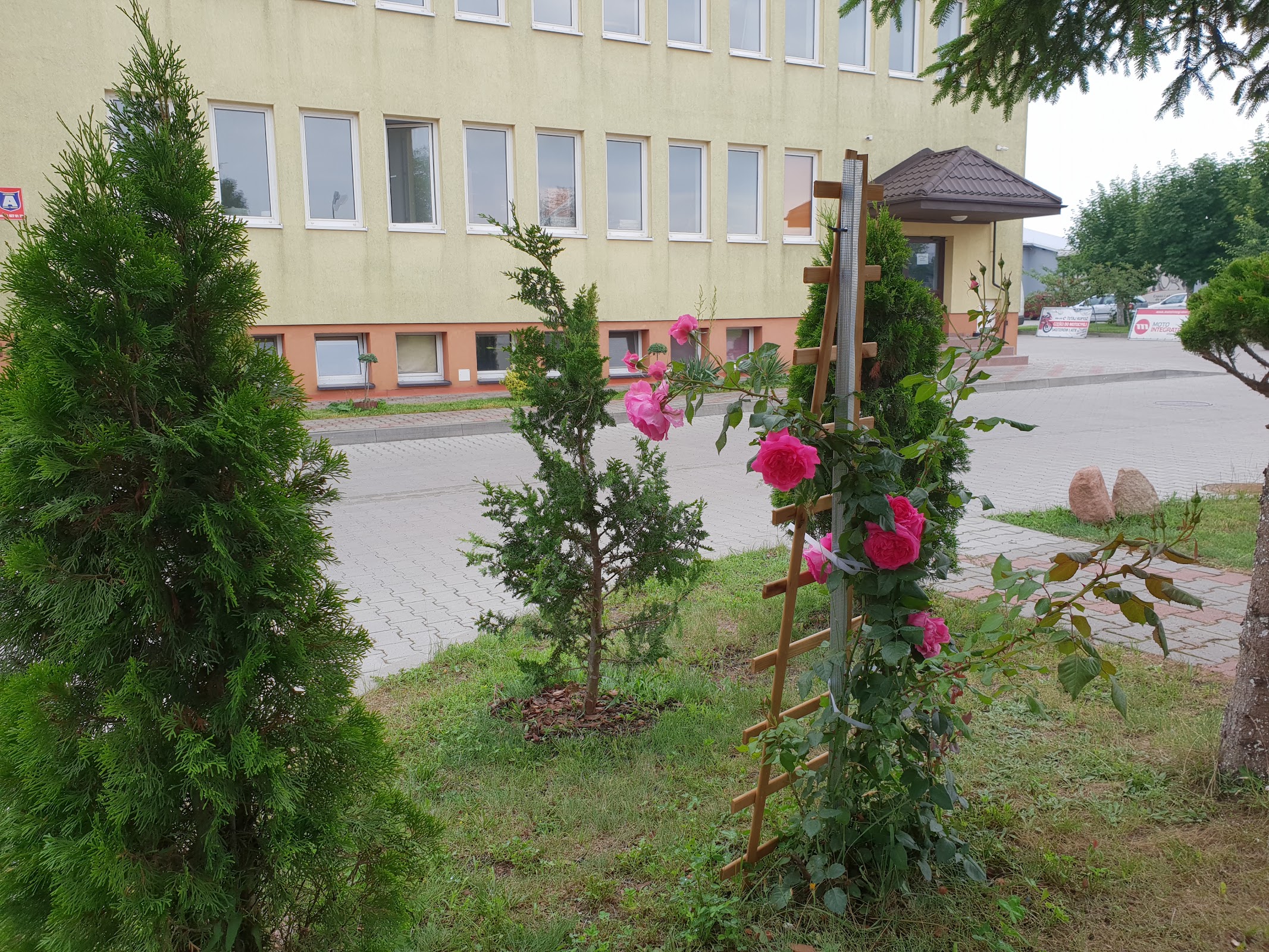Elewacja budynku LUX RESORT w ciągu dnia, róże i tuje przed wejściem