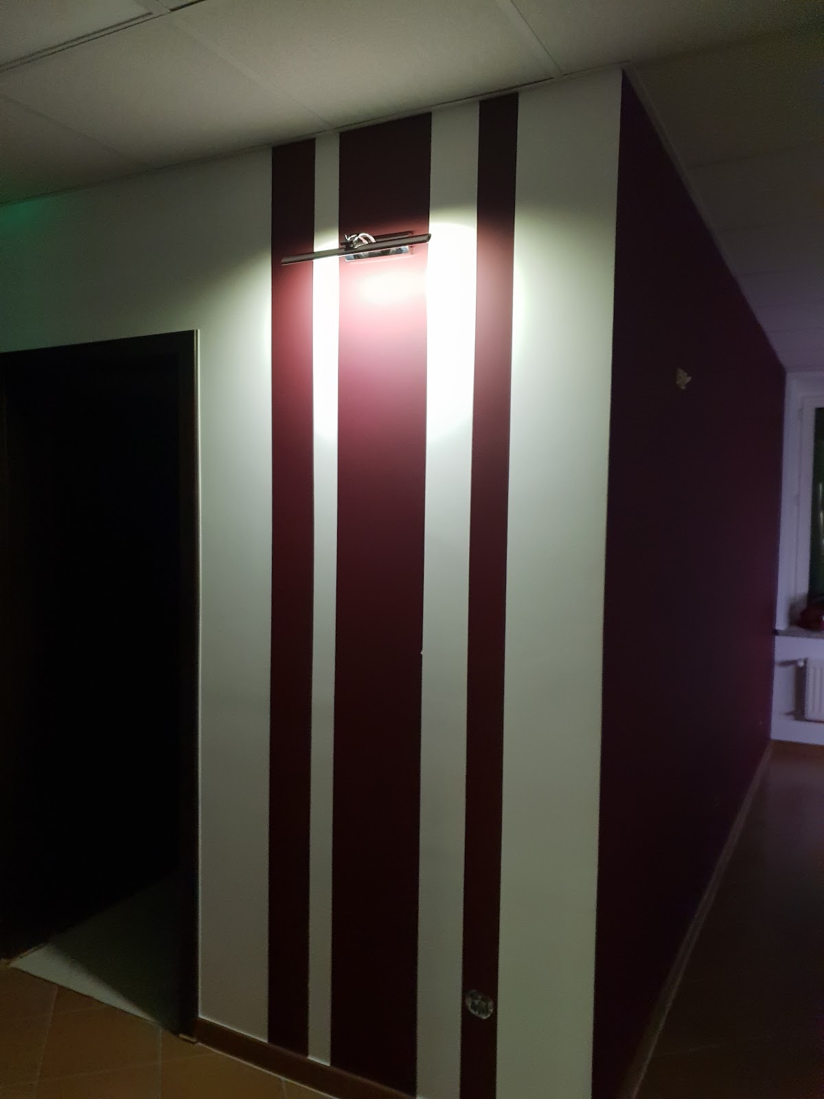 Korytarz z bordowo białymi pasami na ścianie i kinkietem