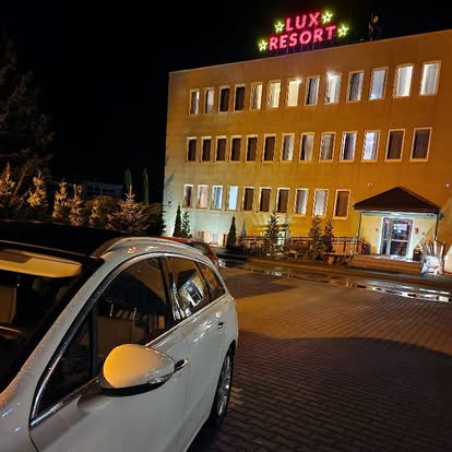 Neon z nazwą LUX RESORT na dachu budynku, widok z parkingu